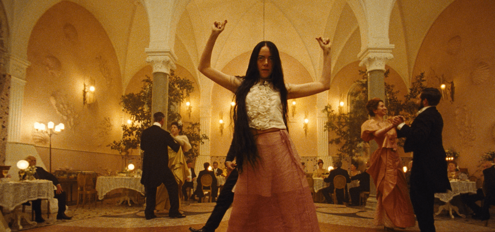 A young, dishevelled woman dances with abandon in a formal ballroom setting