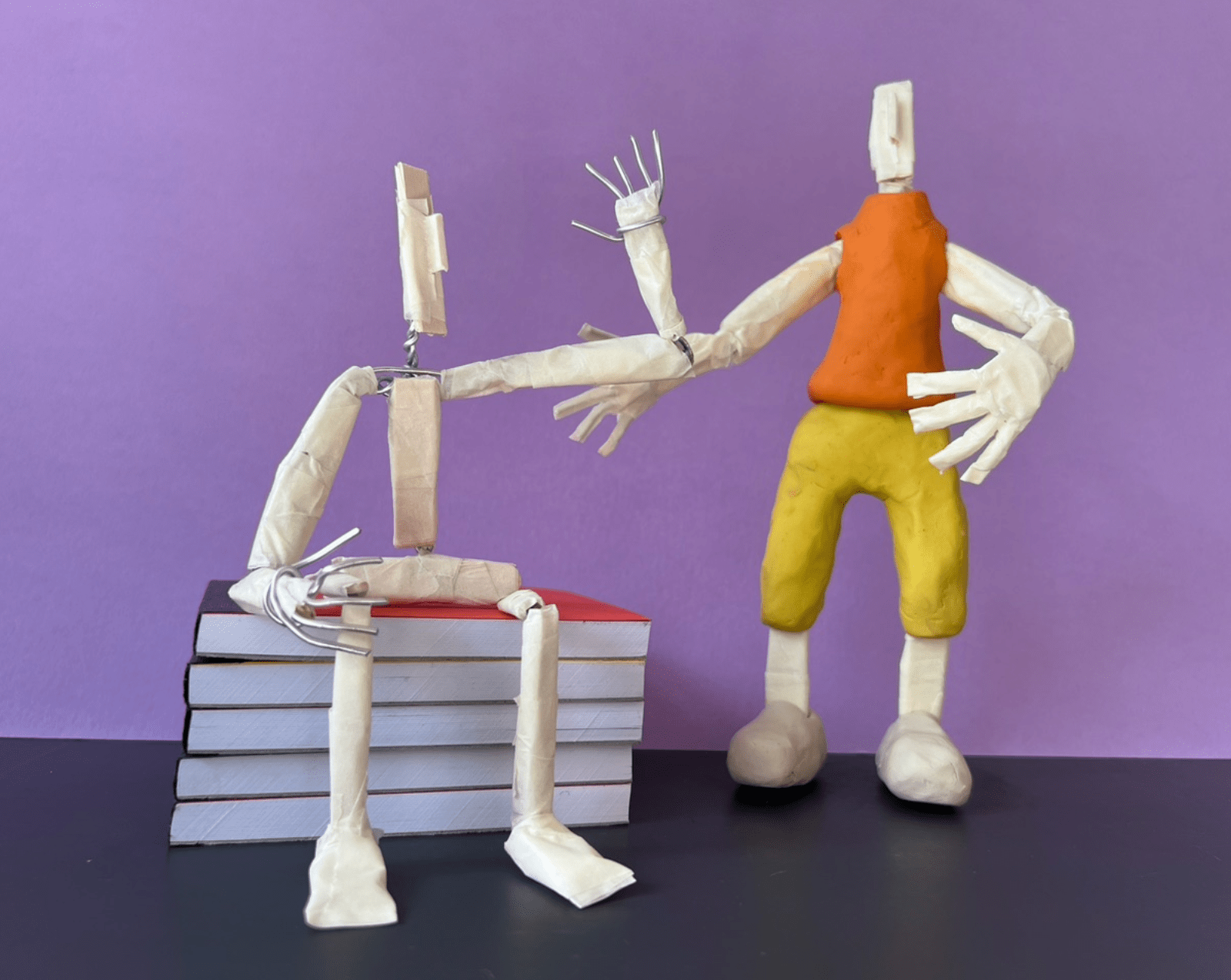 Two characters interacting one sat on books the other above them