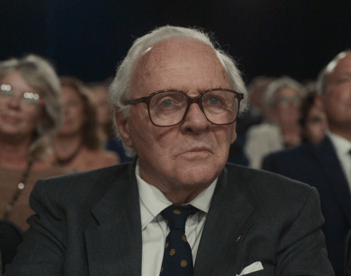 A man in a suit and tie sitting in  the front row of an audience