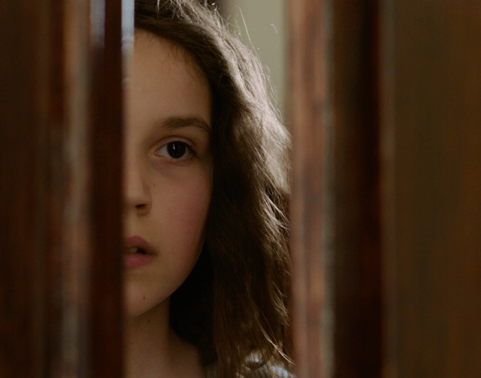 A young girl looks through a door that is ajar