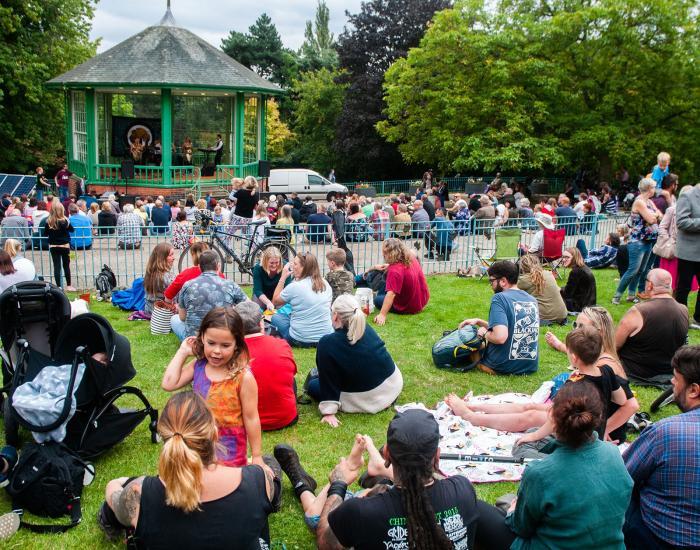 Photo showing a crowd of visitors to Nottingham Green Festival, sitting on grass around a bandstand