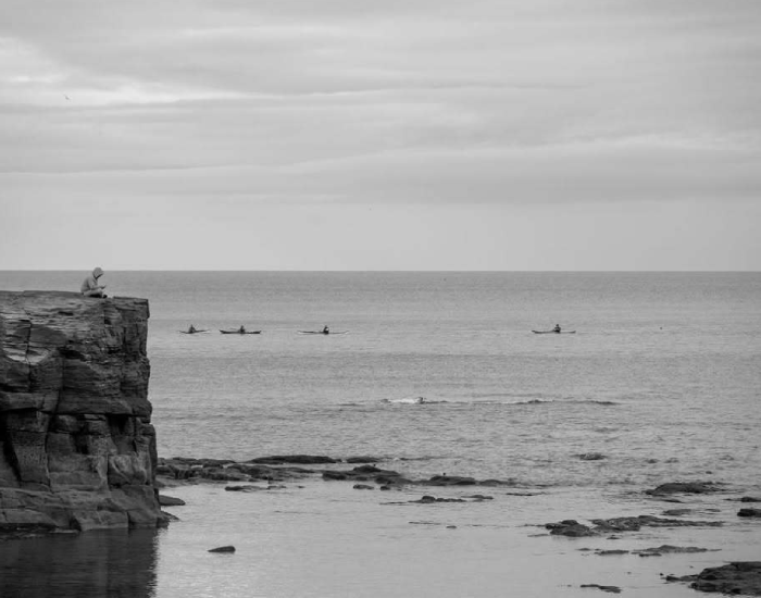 a person sits ontop a cliffs edge above an ocean scape