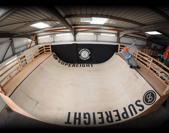 A person on a skateboard with an orange beanie doing a trick at the top of the ramp with Supereight printed on it