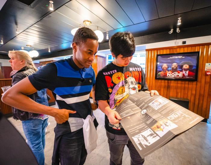Two young people browse Broadway's brochure while standing in the foyer